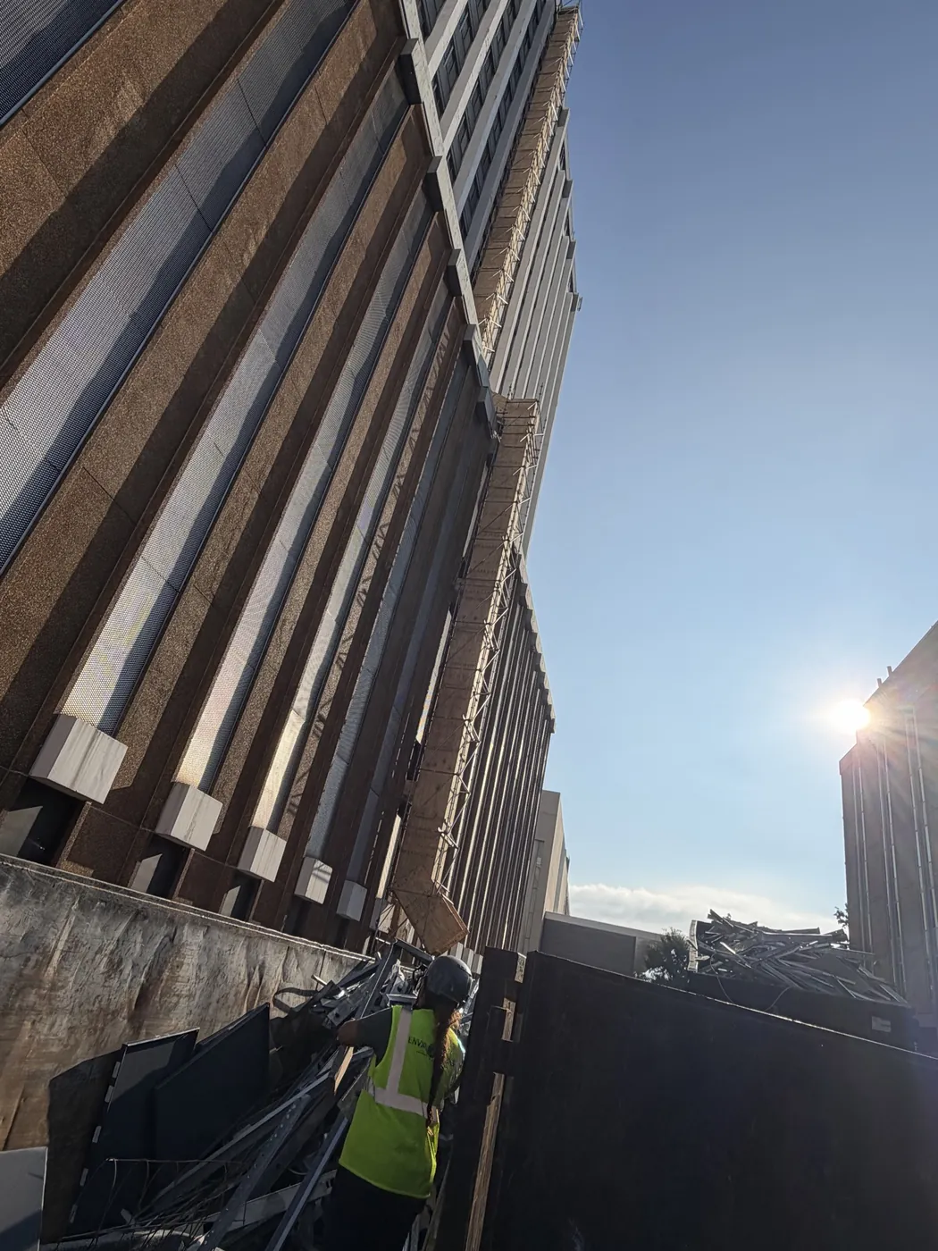 Worker loading metal scrap into a debris container at a high-rise site