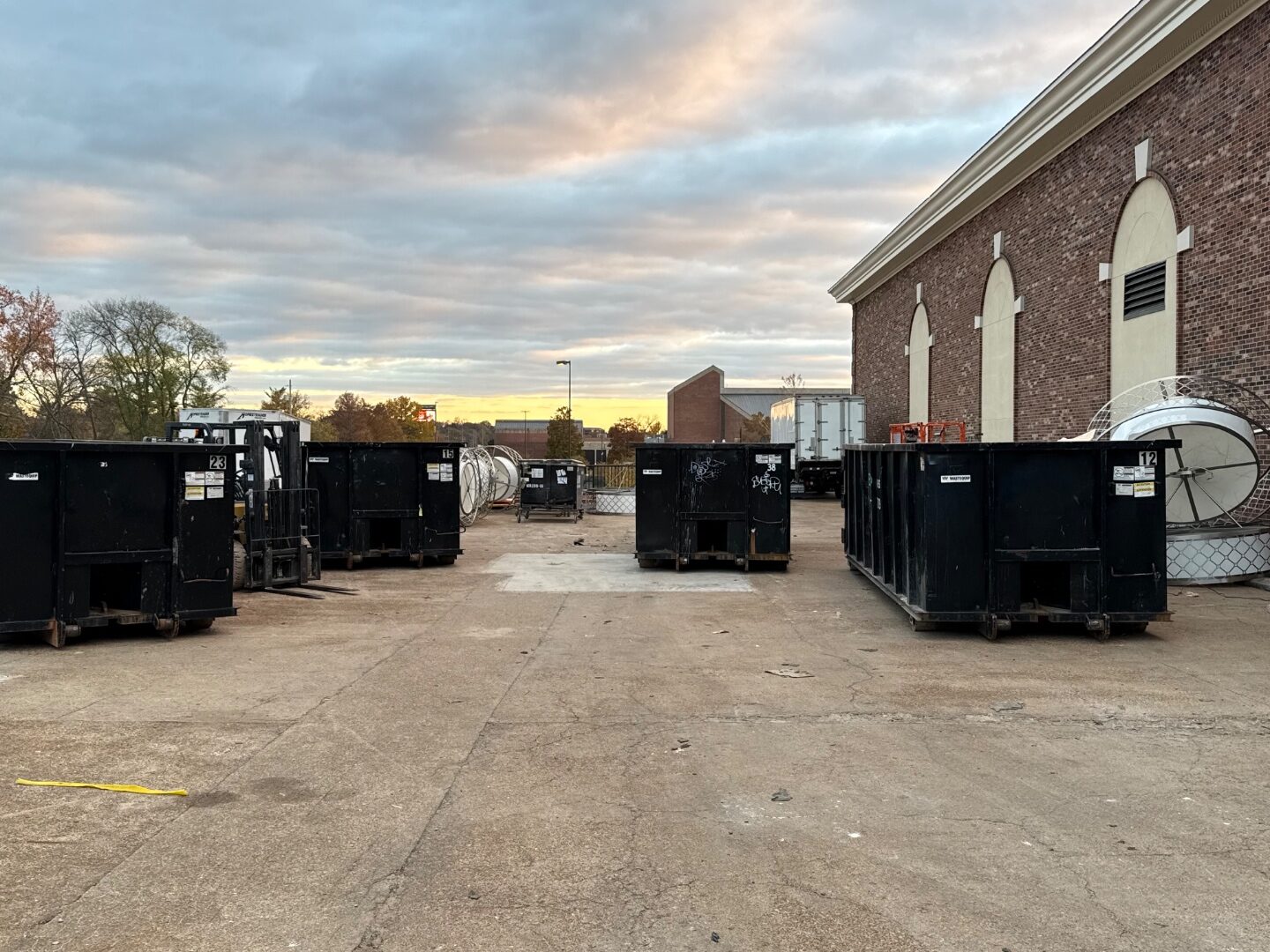 Fleet of black roll-off waste containers staged at sunset